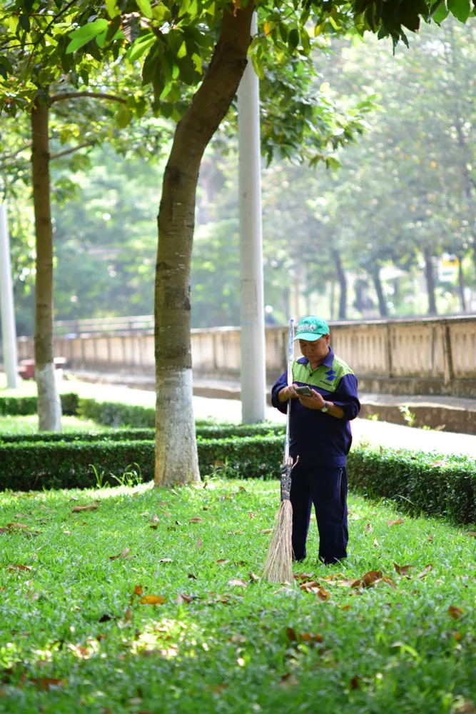 Gardener holding a broom beside fallen leaves on a lawn