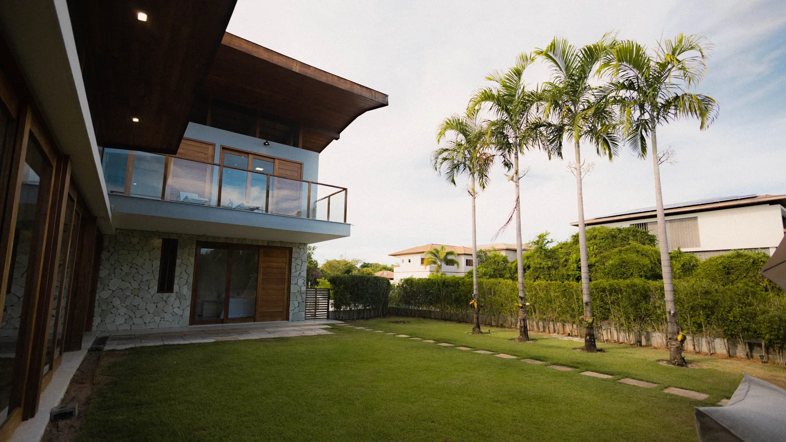 A tropical home with a lawn, palms, and a hedge along the property